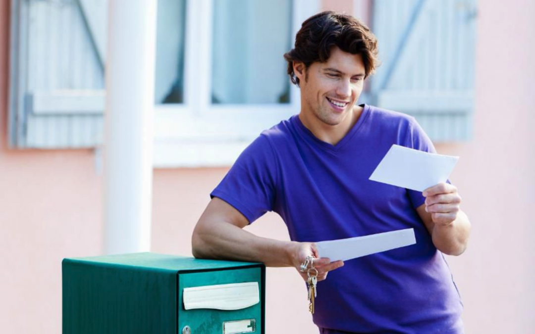 A young man reads mail at his mailbox.